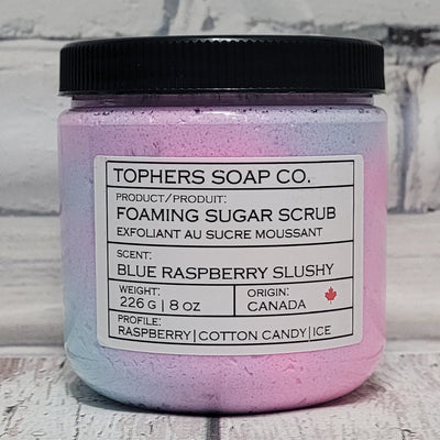 Pink and blue sugar scrub in a clear jar with a black lid against a white brick background