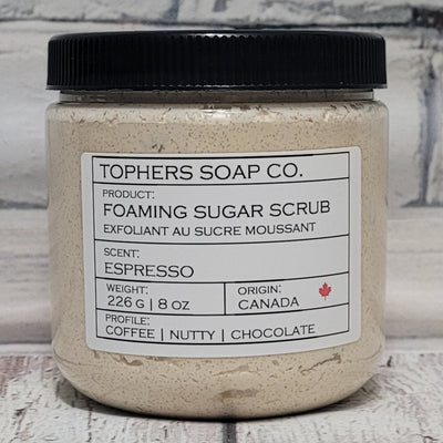 Light tan brown sugar scrub in a clear jar with a black lid against a white brick background