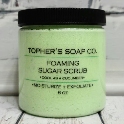 Bright green  sugar scrub in a clear jar with a black lid against a white brick background