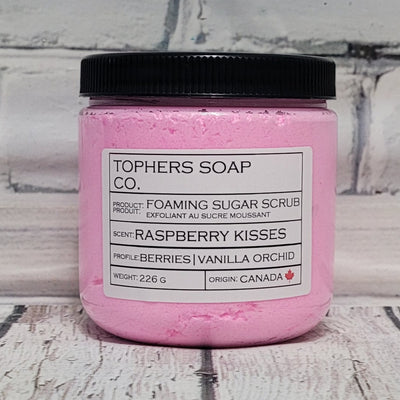 Bubblegum pink  sugar scrub in a clear jar with a black lid against a white brick background
