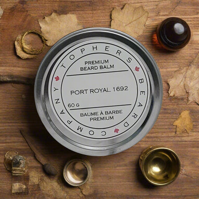 Topher's Beard and Soap Co. Port Royal 1692 Beard Balm – 60 g tin with vintage-inspired label, surrounded by brass, leaves, and aged wood for an old-world pirate aesthetic