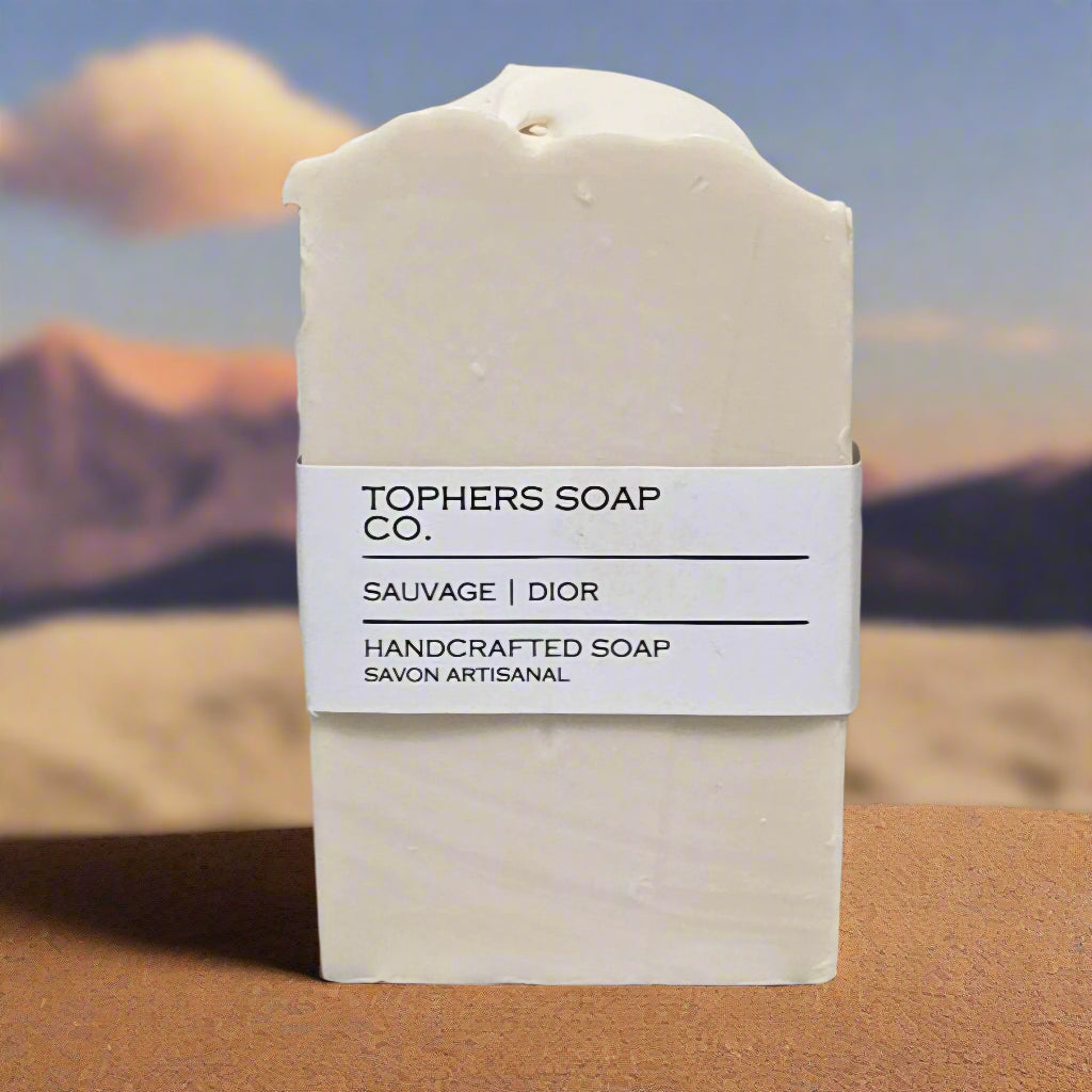 Topher's Beard and Soap Co. Sauvage Dior Handcrafted Soap – creamy white cold process soap bar with minimalist label, set against a desert-inspired background evoking twilight and rugged elegance