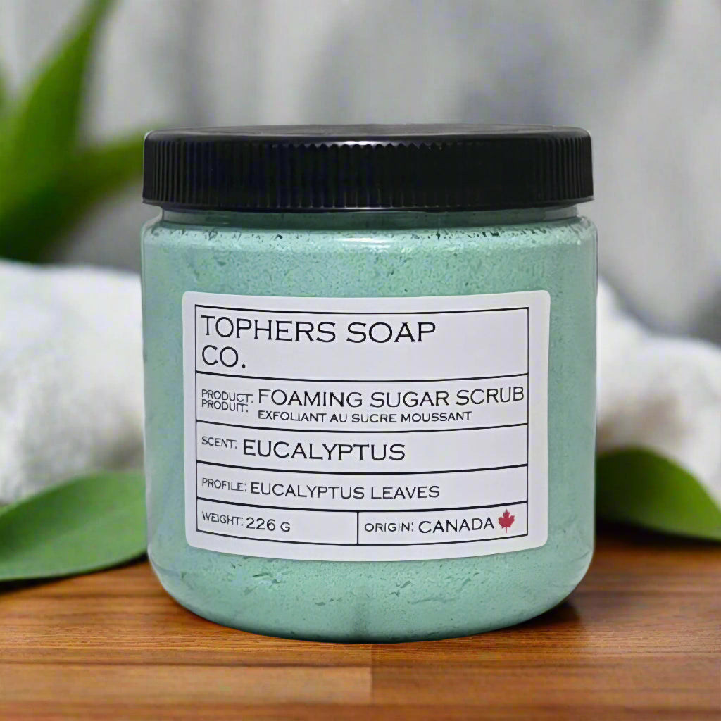 Topher's Beard and Soap Co. Eucalyptus Foaming Sugar Scrub – 226 g jar of green whipped sugar scrub with a fresh eucalyptus scent, styled with natural leaves and spa towels on a wood surface