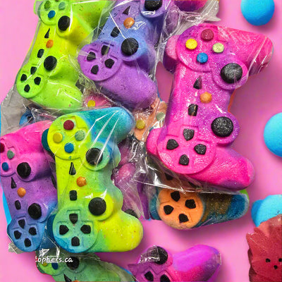 Topher’s Beard and Soap Co. Game Controller Bath Bombs – brightly colored, hand-painted bath bombs shaped like video game controllers in shades of neon pink, purple, blue, green, and yellow, individually wrapped and styled for a fun, gamer-themed bath experience.

