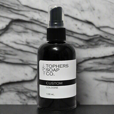 Topher’s Beard and Soap Co. Custom Cologne – 126 ml black cologne bottle with a minimalist label, displayed in front of a white and gray marble backdrop to emphasize premium quality and personalization.