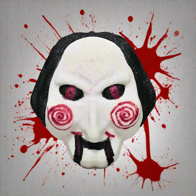 Topher’s Beard and Soap Co. Billy the Puppet Bath Bomb – hand-painted bath bomb inspired by the SAW movie franchise, featuring the puppet’s iconic white face with red spiral cheeks and black hair, displayed against a backdrop of dramatic blood splatter for a horror-themed presentation.