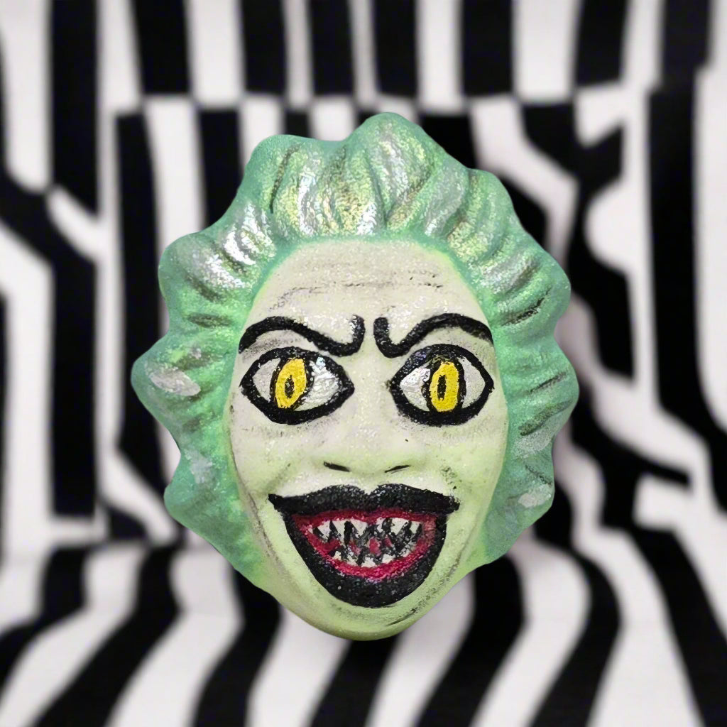 Topher’s Beard and Soap Co. Beetlejuice Bath Bomb – hand-painted bath bomb featuring a green-haired, sharp-toothed character design inspired by Beetlejuice, set against a black and white striped background to reflect the film’s iconic visual style.

