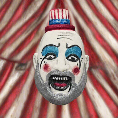 Topher’s Beard and Soap Co. Captain Spaulding Bath Bomb – hand-painted horror-inspired bath bomb depicting the character from Rob Zombie’s films, displayed against a filthy red and white circus tent backdrop to evoke a gritty, unsettling carnival atmosphere.