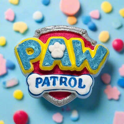 Topher’s Beard and Soap Co. Paw Patrol Bath Bomb – hand-painted bath bomb shaped like the Paw Patrol logo, styled on a tiled surface with bath toys and bubbles for a playful, kid-friendly presentation.