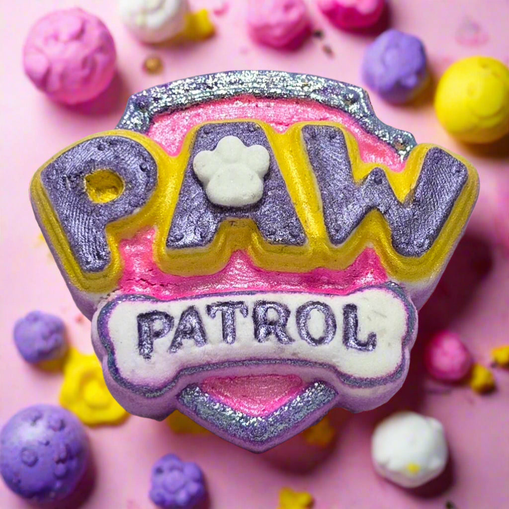 Topher’s Beard and Soap Co. Pink and Purple Paw Patrol Bath Bomb – hand-painted bath bomb shaped like the Paw Patrol logo in pink and purple, displayed on a pastel tile surface with playful bath props and bubbly accents.