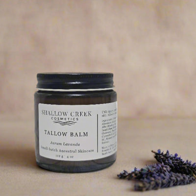 A 4 oz jar of Shallow Creek Cosmetics Tallow Balm, Aurum Lavanda, an ancestral skincare product, displayed on a warm background with dried lavender flowers, emphasizing its natural formulation.