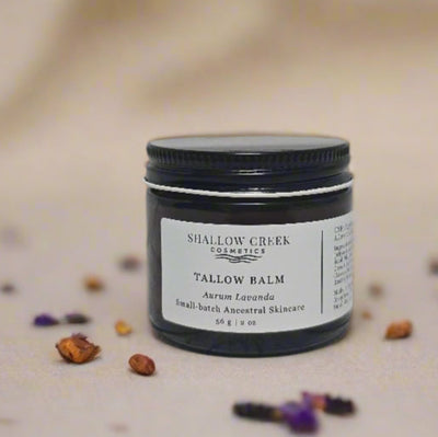 A jar of Shallow Creek Cosmetics Tallow Balm, Aurum Lavanda, an ancestral skincare product, displayed with small botanical elements on a light background.
