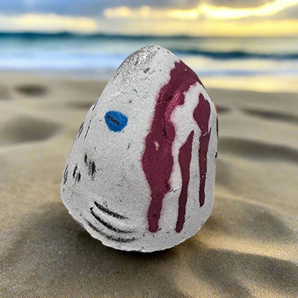 Hand-painted Shark Bite Bath Bomb by Topher's Beard and Soap Co. on a weathered wooden dock background with peeling blue paint, resembling a shark attack scene.
