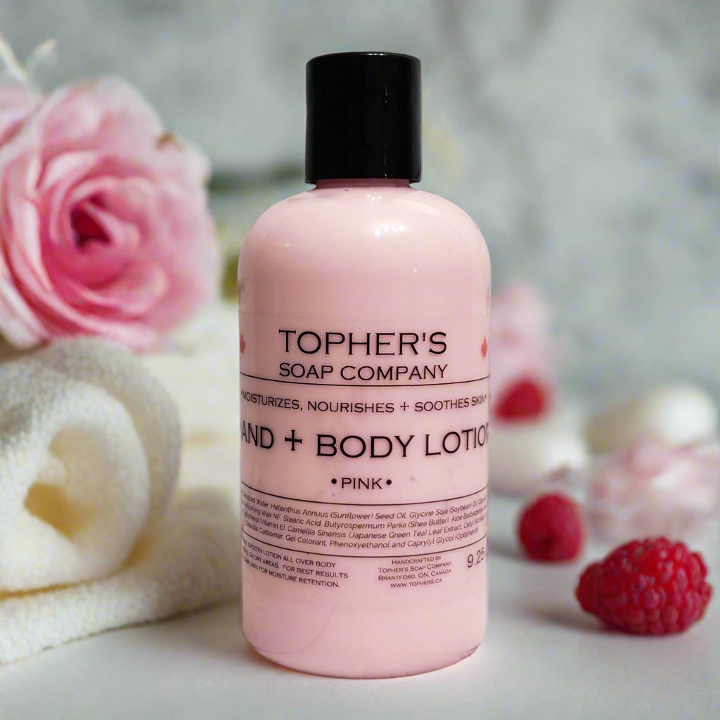 Tophers Soap Co. Pink Sugar Hand and Body Lotion in a pink bottle with a black cap, surrounded by pink roses and raspberries.
