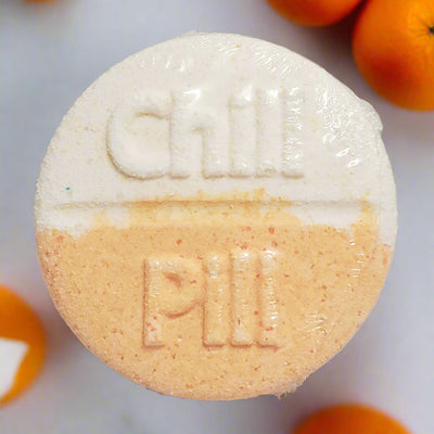 Large, round bath bomb from Tophers Soap Co. in Brantford, Ontario, divided into a textured white top half with "Chill" embossed and a textured orange bottom half with "Pill" embossed, surrounded by fresh oranges, showcasing a fun and locally handcrafted bath treat reminiscent of a classic creamsicle.