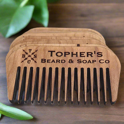 Stack of smooth, laser-cut cherry wood beard combs from Tophers Beard & Soap Co., engraved with the company logo, showcasing the craftsmanship of this locally made product from Brantford, Ontario.