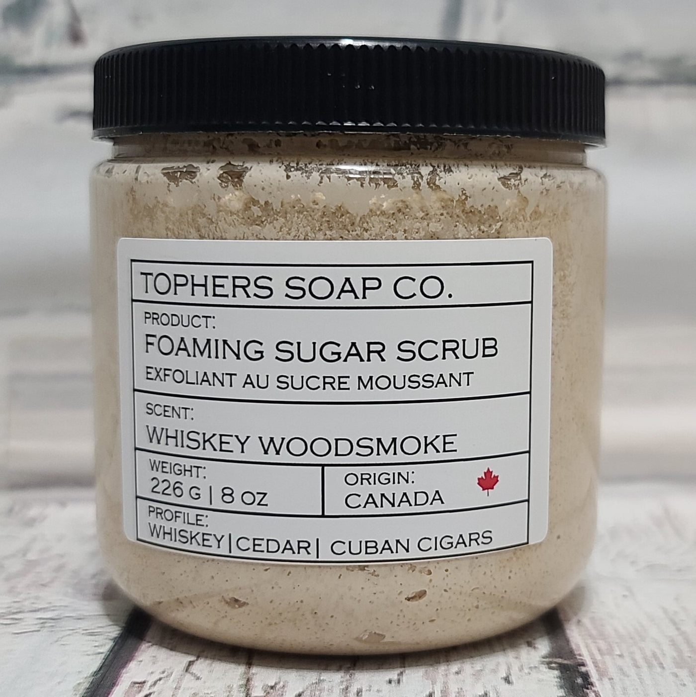Creamy brown  sugar scrub in a clear jar with a black lid against a white brick background