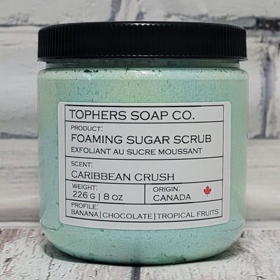Blue and Green sugar scrub in a clear jar with a black lid against a white brick background