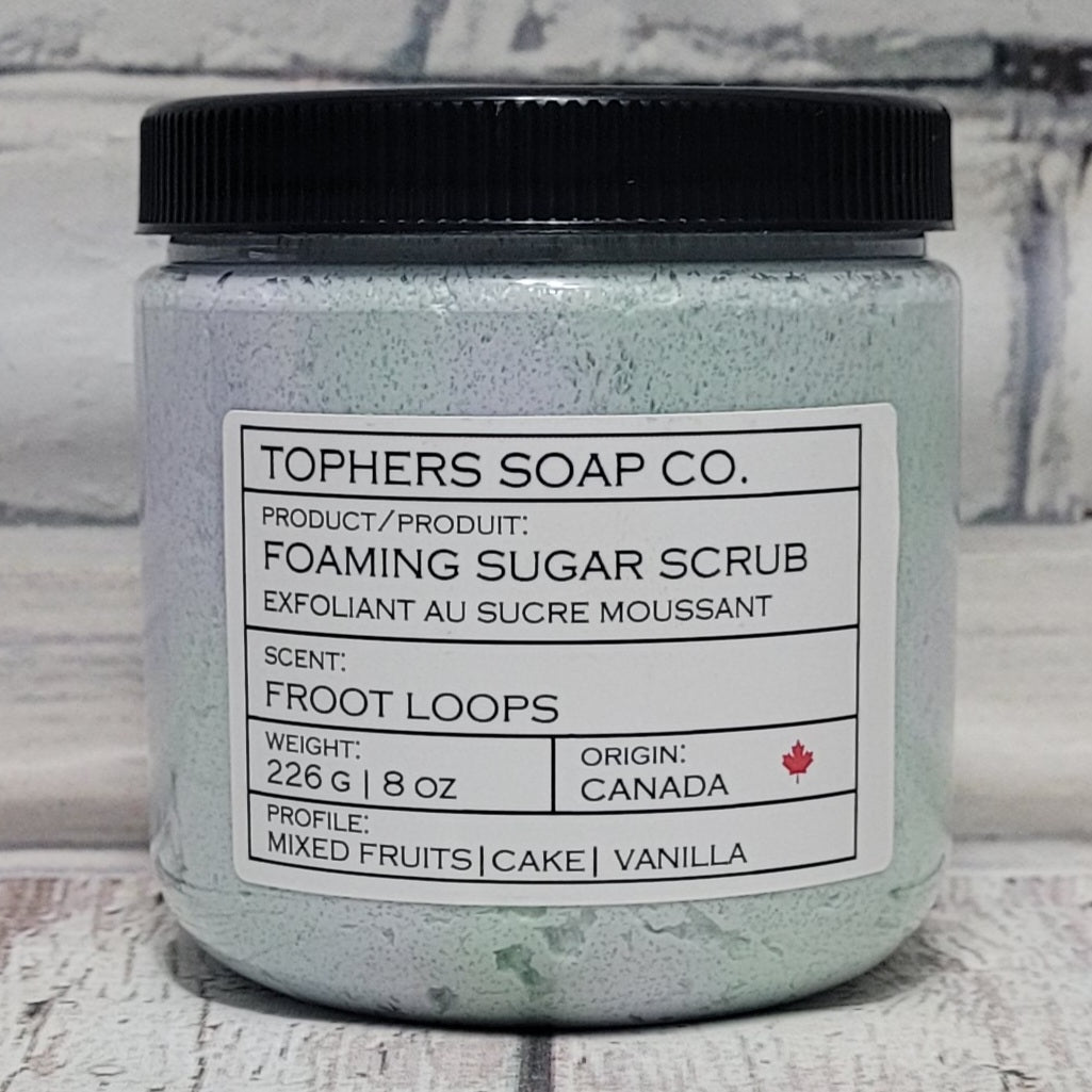 Green and purple sugar scrub in a clear jar with a black lid against a white brick background