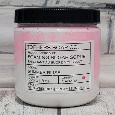 Pink and White  sugar scrub in a clear jar with a black lid against a white brick background