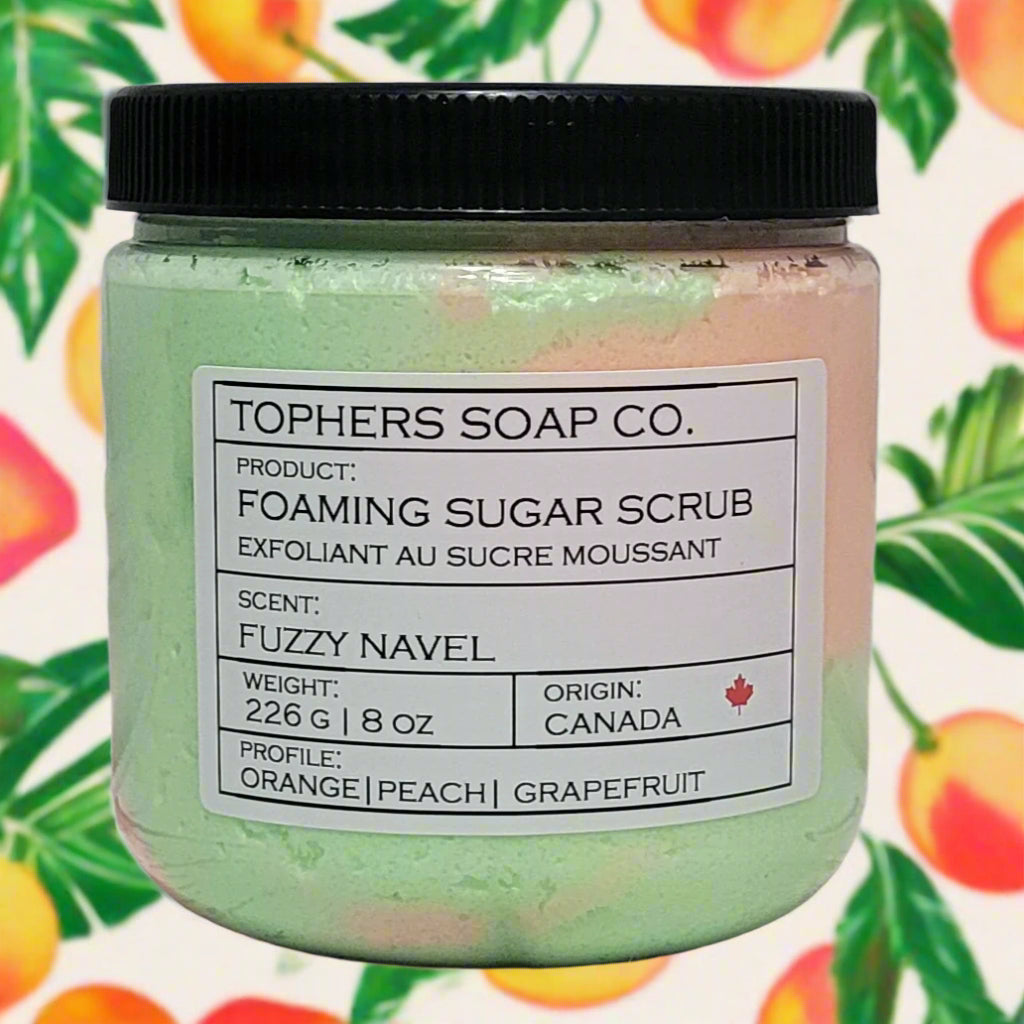 Orange and green sugar scrub in a clear jar with a black lid against a white brick background