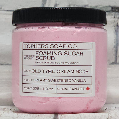 Cotton Candy Pink sugar scrub in a clear jar with a black lid against a white brick background