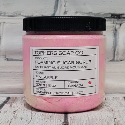 Pink and yellow  sugar scrub in a clear jar with a black lid against a white brick background