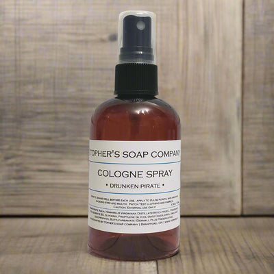 Dark bottle of Tophers Beard Co. Drunken Pirate Cologne Spray with a clear spray nozzle and a white label featuring its Bay Rum and citrus scent profile, photographed against a rustic wooden background, emphasizing its creation in Brantford, Ontario, Canada.