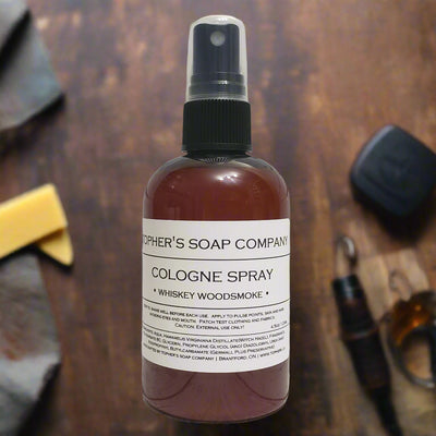 Dark bottle of Tophers Beard Co. Whiskey Woodsmoke Cologne Spray with a clear spray nozzle and a white label detailing its whiskey, cigar, and wood scent profile, photographed with elements suggesting whiskey and wood, emphasizing its creation in Brantford, Ontario, Canada.