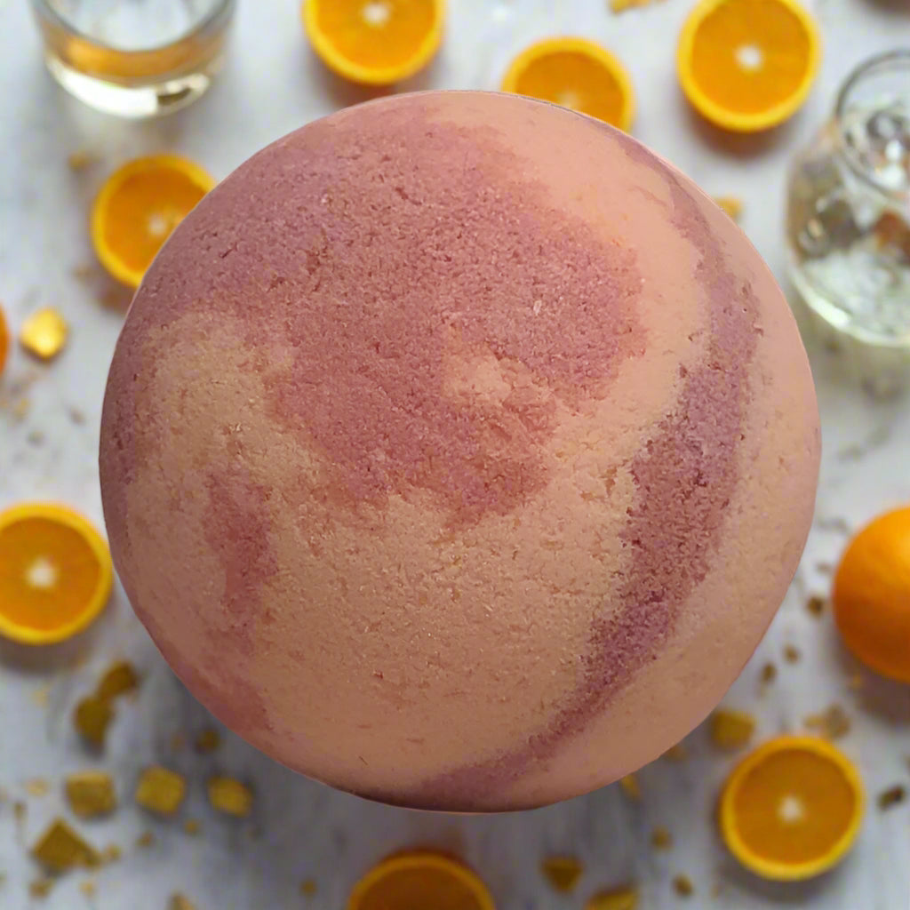 Pink and orange swirl bath bomb, likely the Mimosa scent, surrounded by orange slices and champagne glasses in Brantford, Ontario. Tophers Soap Co.