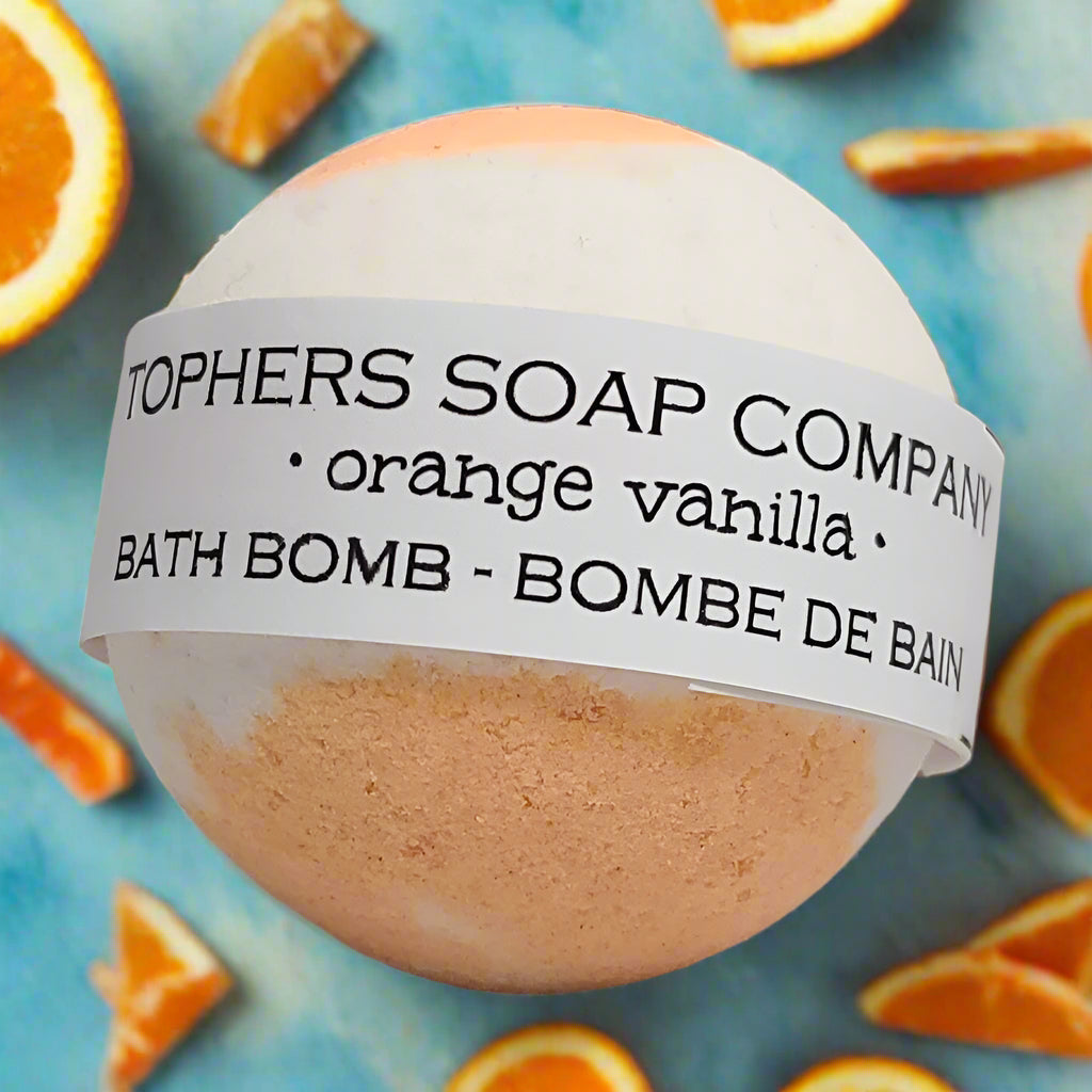 Topher's Soap Company Orange Vanilla Bath Bomb - A white and orange swirl bath fizzer with a label clearly indicating the "orange vanilla" scent, surrounded by slices of orange.